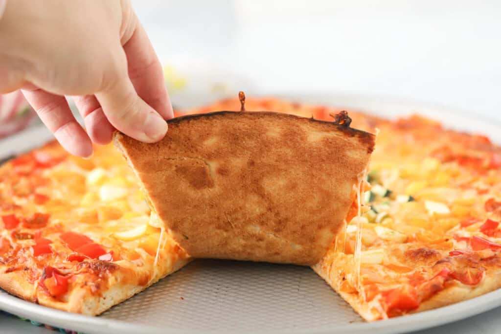 A hand grabbing a slice of baked veggie pizza.
