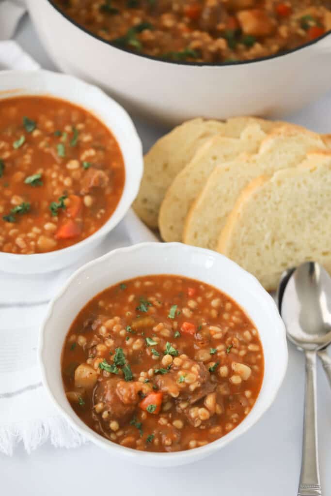 Beef and barley soup in bowls with a side of sliced bread.