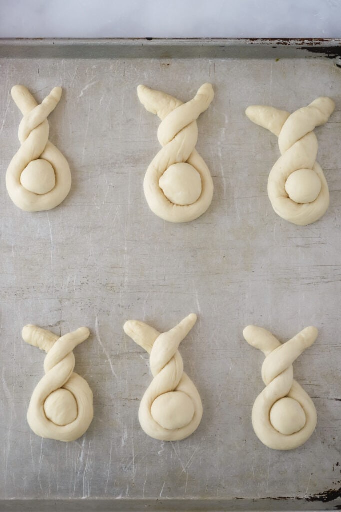 a baking sheet with dough shaped into easter bunny rolls. 