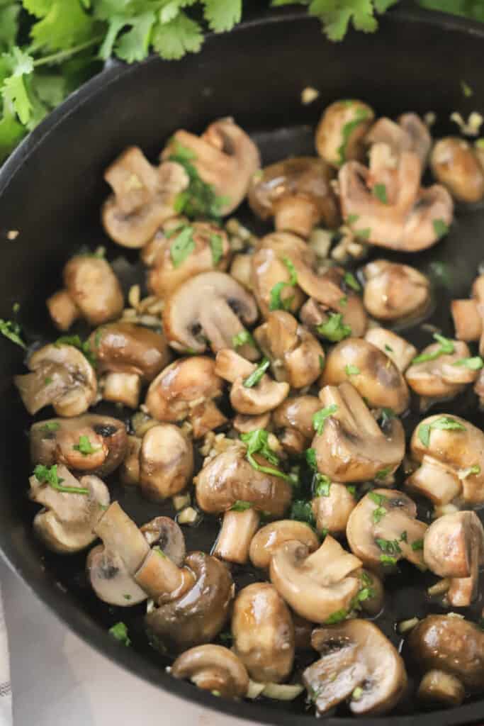 A cast iron skillet cooking sauteed garlic butter mushrooms, an easy side dish recipe.