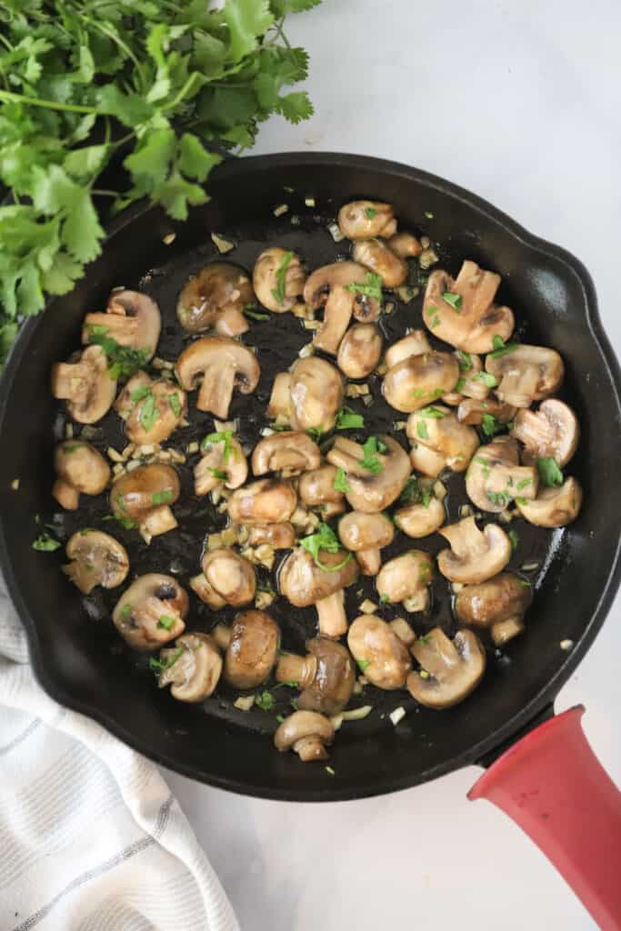 A skillet with sauteed mushrooms cooking in garlic butter sauce and topped with fresh herbs.
