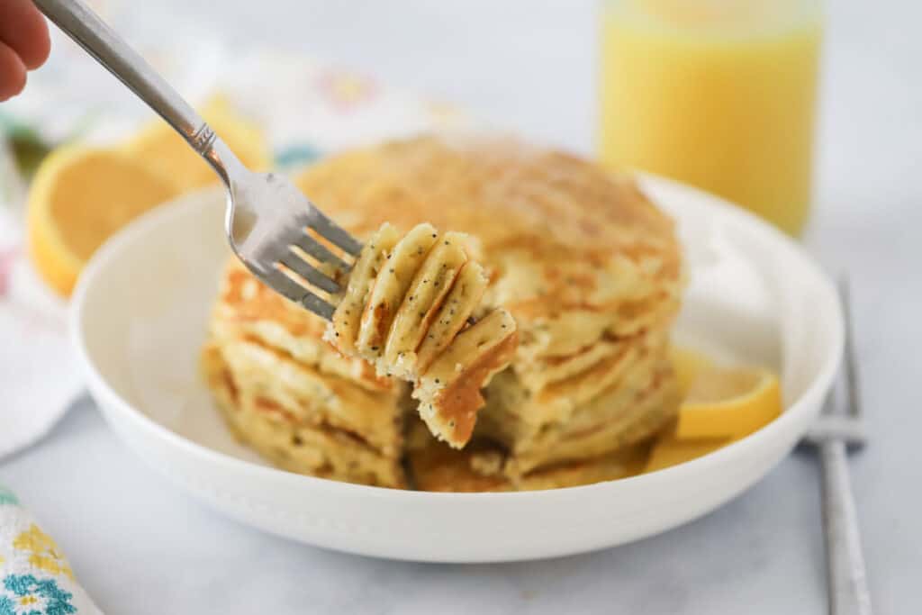 A fork digging into lemon pancakes with poppy seeds and maple syrup.