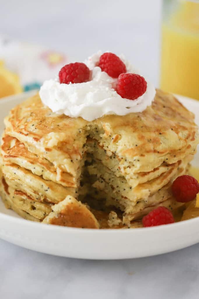 A stack of Lemon Poppy Seed Pancakes topped with whipped cream and raspberries.