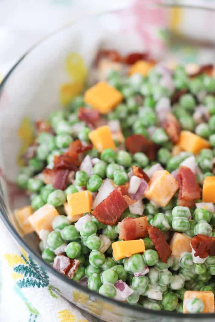 A large bowl full of pea salad with bacon, cheddar cheese, red onions, and ranch dressing.