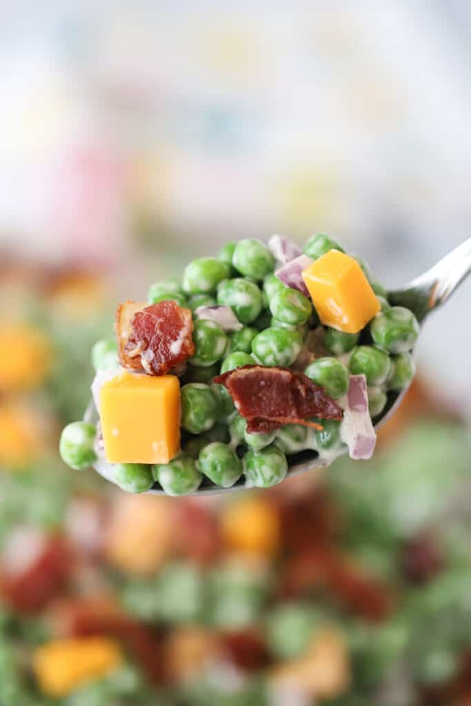 A spoon full of this recipe for pea salad with bacon, topped with chunks of cheddar cheese.
