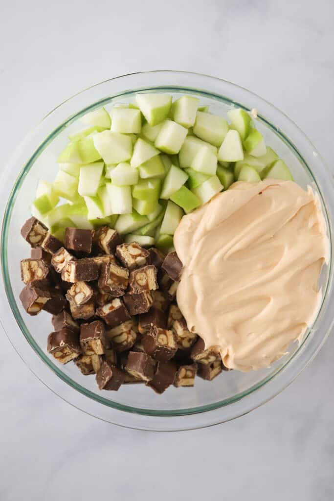 Granny smith apples, diced Snickers bars, and instant pudding in a bowl to make apple fruit salad with snickers.