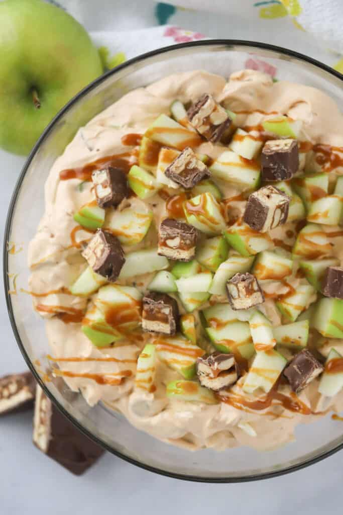 Apple salad with Snickers in a large bowl topped with caramel sauce.