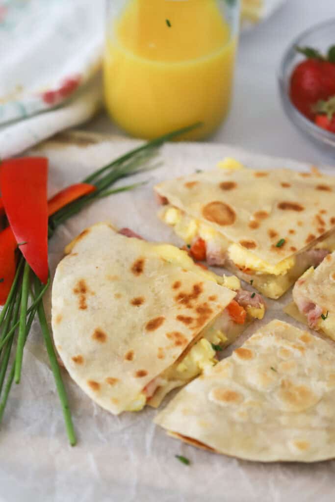 A serving plate with a breakfast quesadilla cut into quarters.