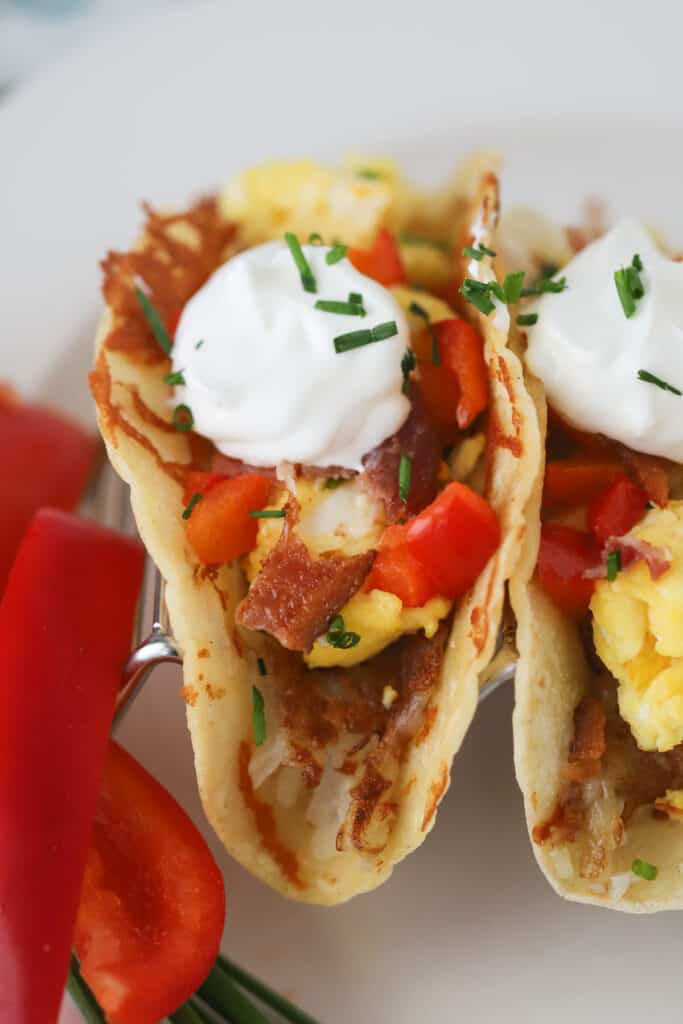 A breakfast taco filled with scrambled eggs, bacon, peppers, and topped with sour cream and chives all in a corn tortilla.