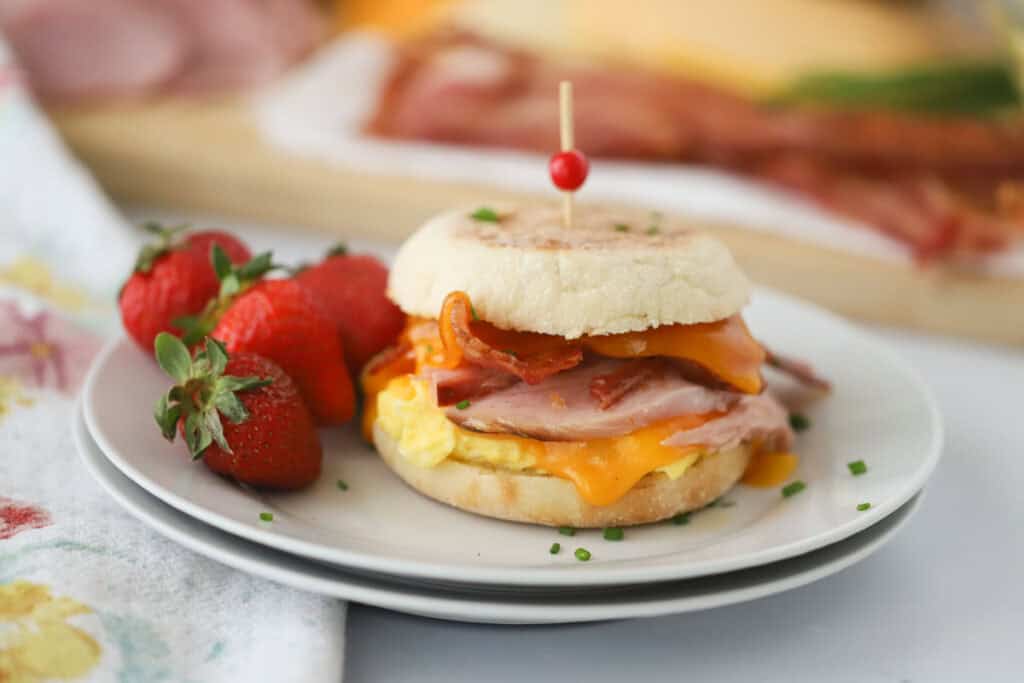A plate with an egg mcmuffin breakfast sandwich and some fresh strawberries.
