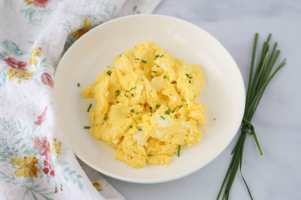 A serving bowl full of perfect scrambled eggs topped with fresh chives.