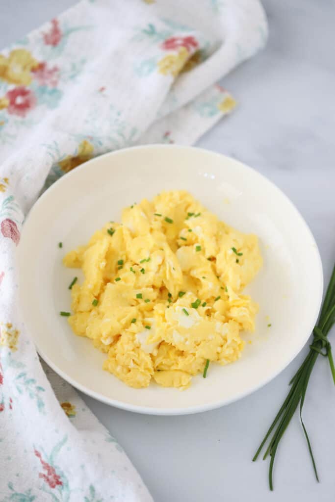 A bowl full of fluffy scrambled eggs topped with fresh chives.