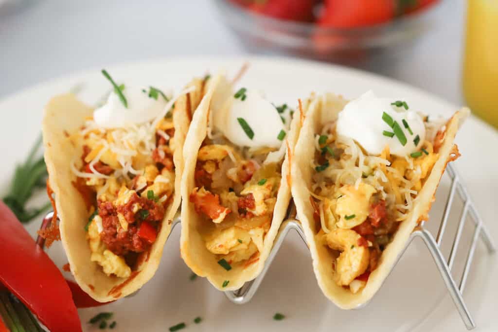 A taco holder with mexican breakfast tacos, filled with chorizo, scrambled eggs, potatoes, and green chilis.