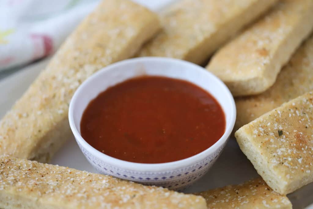 Freshly baked homemade breadsticks with a bowl of marinara sauce for dipping.