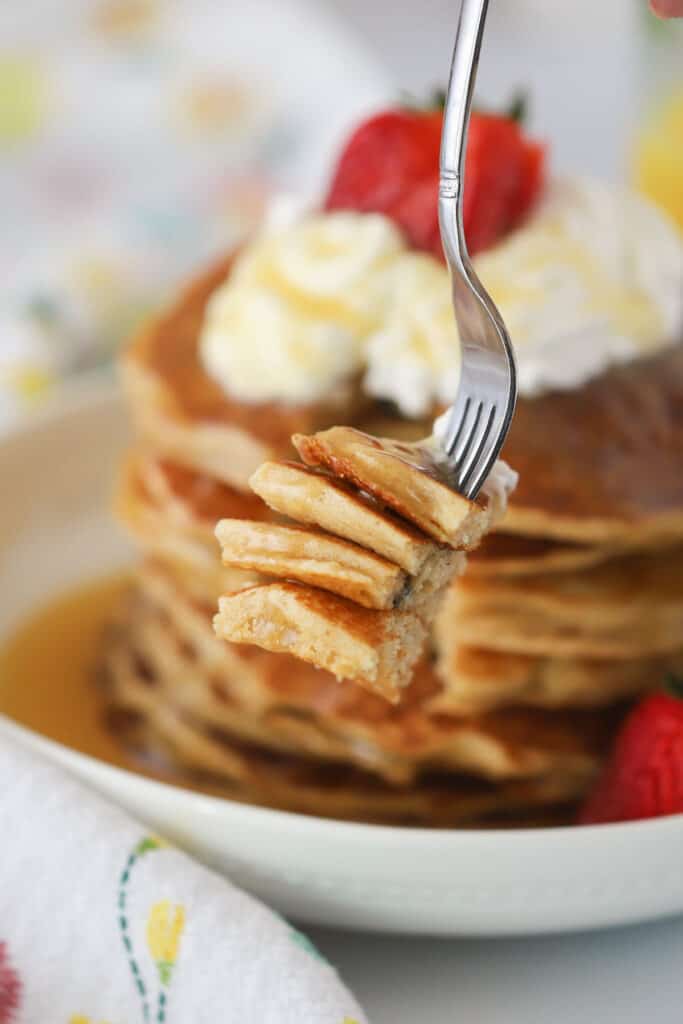 A fork with a stack of pancakes topped with whipped cream and strawberries.