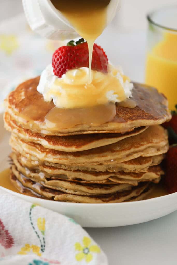A tall stack of whole wheat flour pancakes with syrup being poured over.