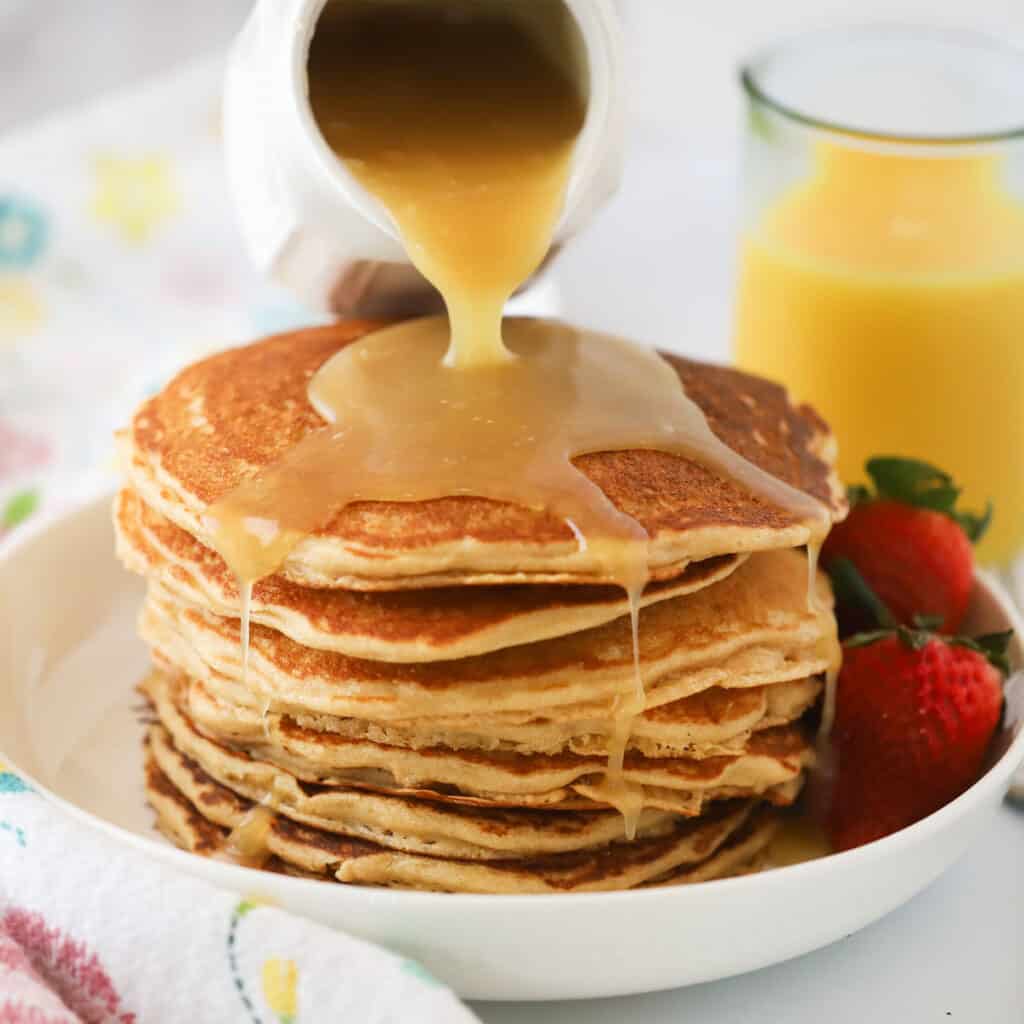 A plate of pancakes with coconut buttermilk syrup being poured over the top.