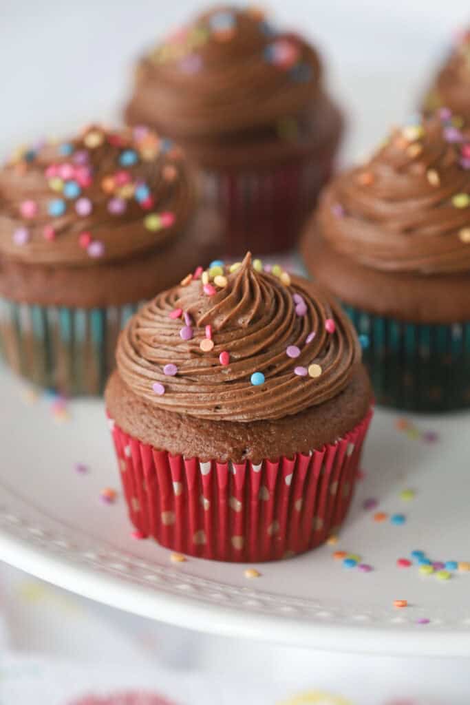 Chocolate cupcakes topped with chocolate cream cheese frosting and colorful sprinkles.