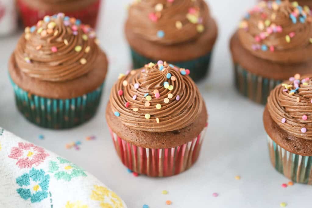 A table with chocolate cupcakes decorated with piped cream cheese and chocolate icing and sprinkles.