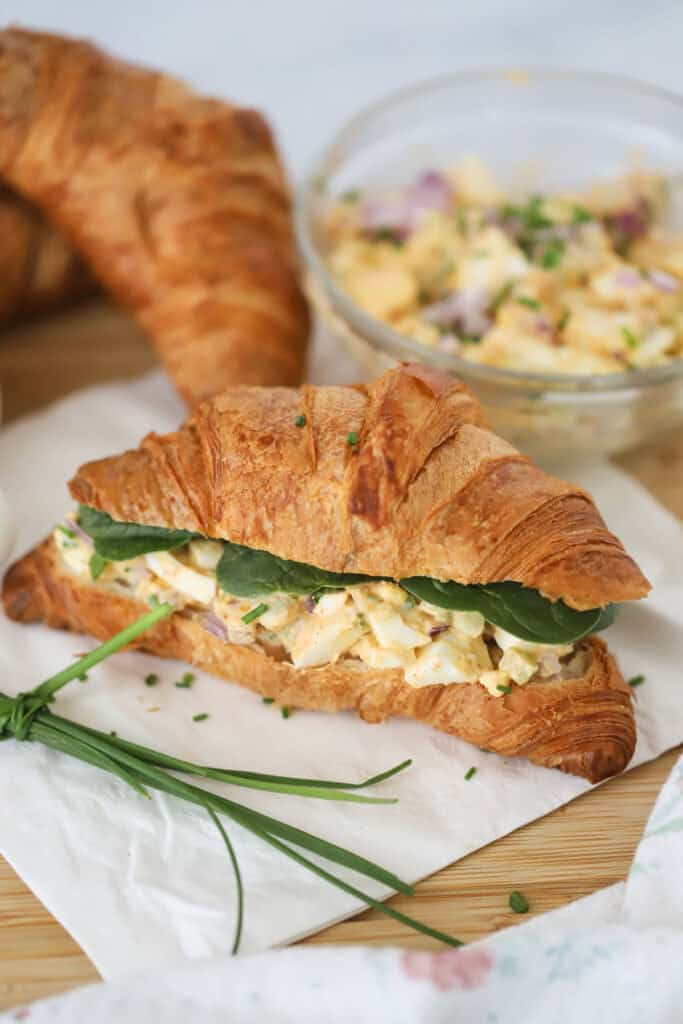 A countertop with the best egg salad sandwich recipe served on a croissant.
