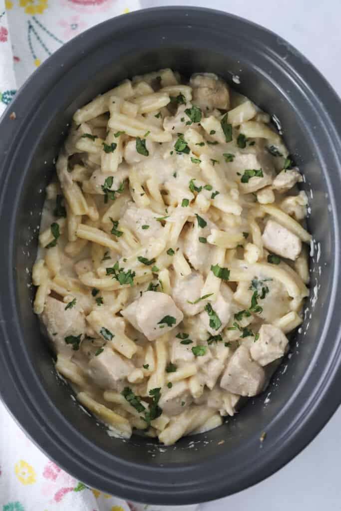 A crockpot full of lemon and thyme chicken pasta, garnished with fresh parsley.