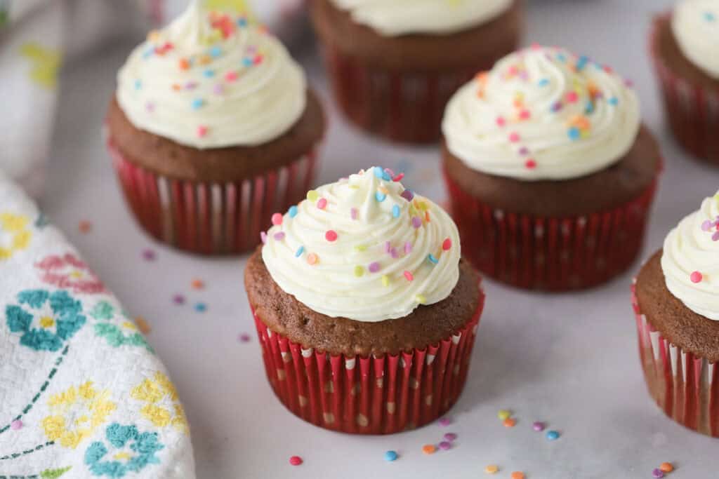Chocolate cupcakes on a table with white chocolate cream cheese frosting piped on top.