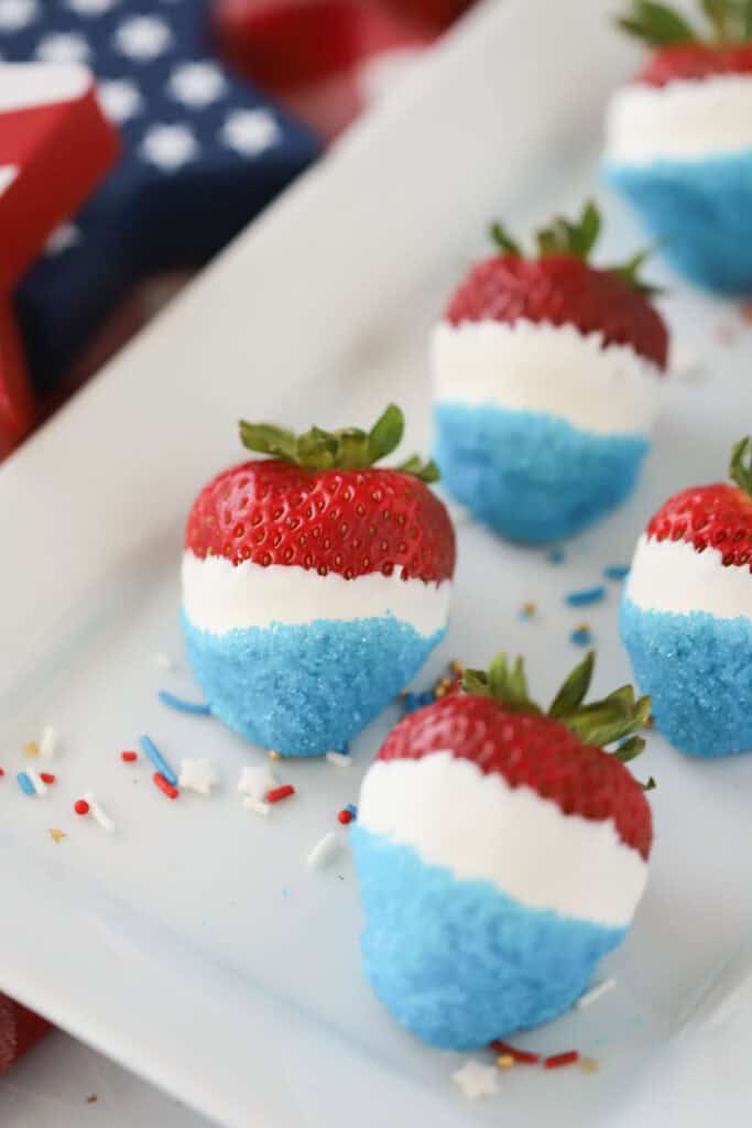 A tray of white chocolate covered strawberries dipped in blue sanding sugar.