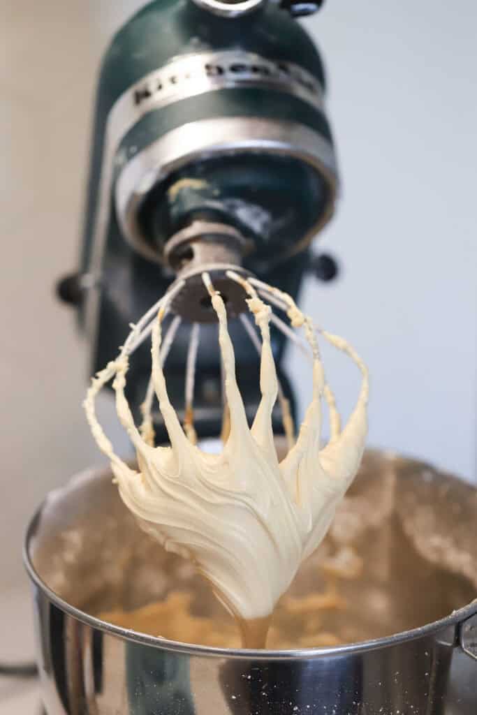 A stand mixer with the whisk attachment full of whipped caramel frosting.