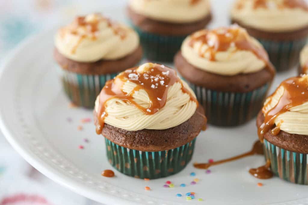 A plate with chocolate cupcakes topped with this caramel icing recipe and a drizzle of salted caramel sauce.