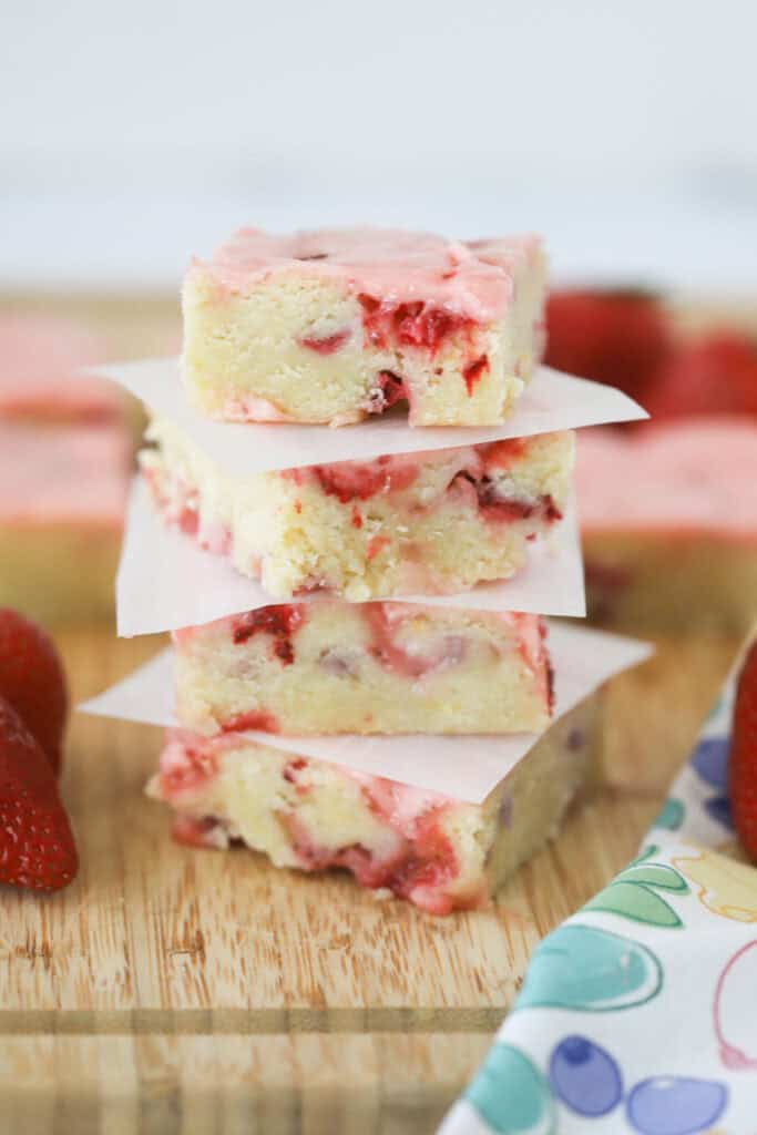 A stack of strawberry blondies with pink frosting and diced strawberries all throughout.