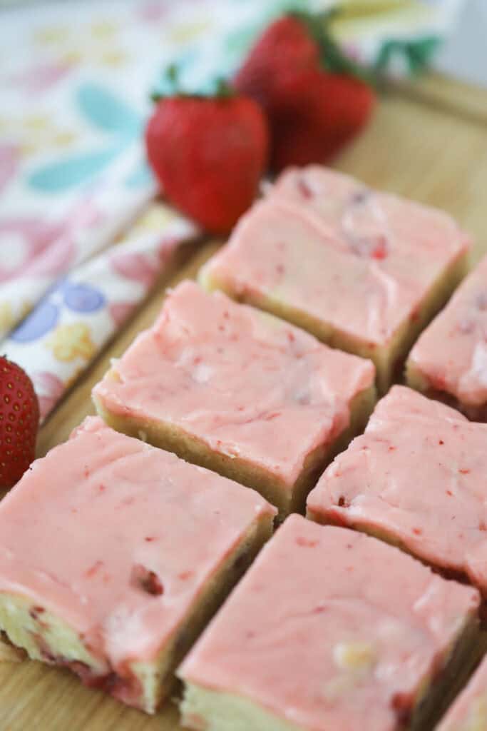 Strawberry blondie squares on a cutting board topped with pink icing.