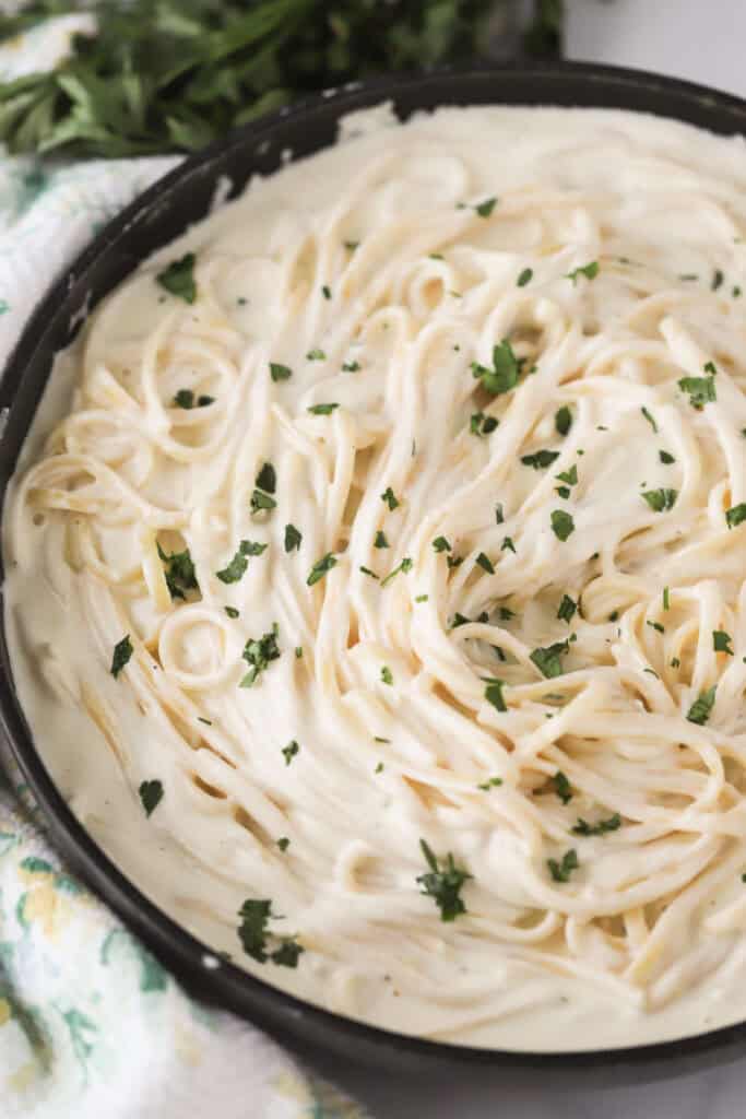 Fettuccine pasta in a pan covered with asiago alfredo sauce.