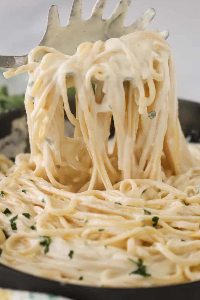 A large spoon pulling out fettuccine pasta noodles covered with asiago alfredo cream sauce.