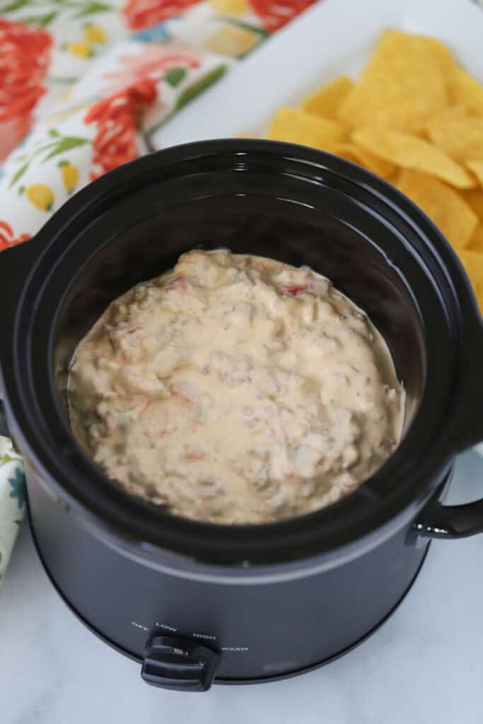 A crockpot full of this cheesy sausage dip recipe with a bowl of tortilla chips beside for dipping.