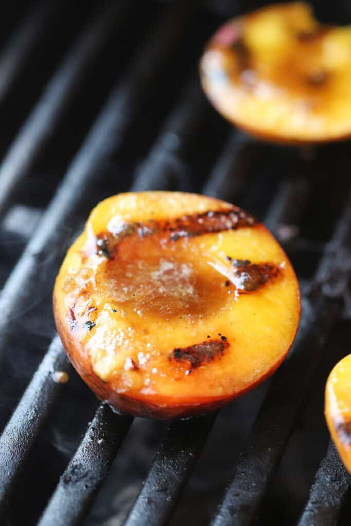 Grilled peaches cooking on a grill with a butter and brown sugar glaze melting over the top.