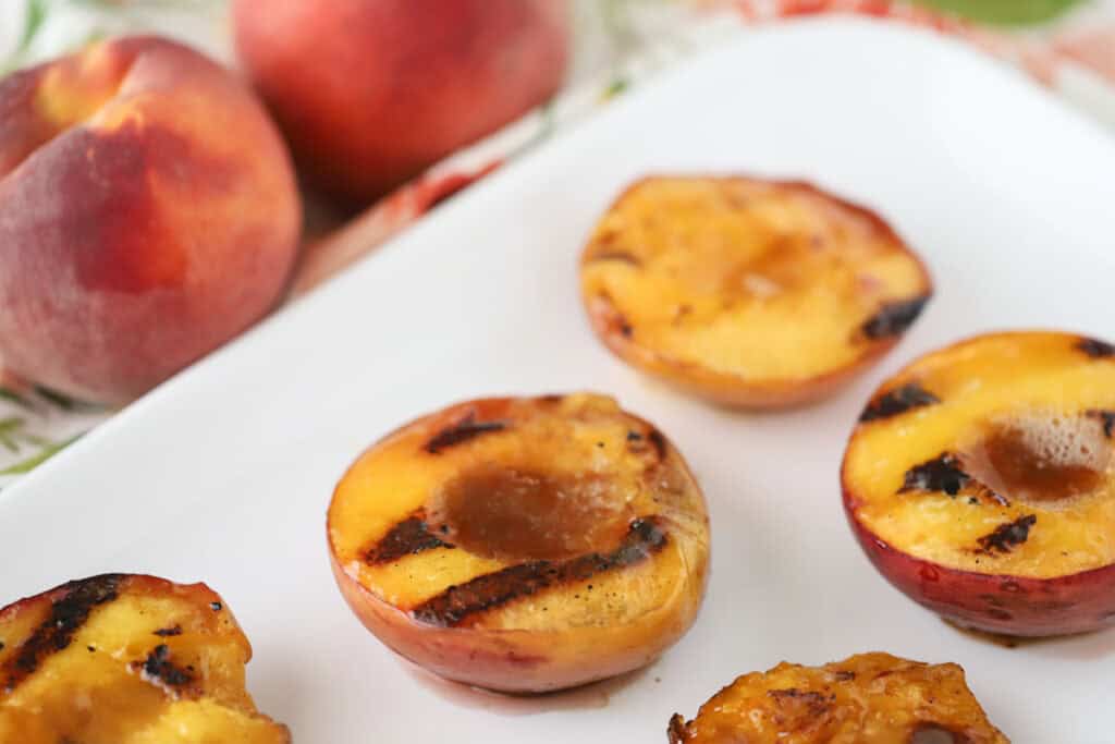 A platter with peaches from this grilled peaches recipe, topped with buttery brown sugar and cinnamon.