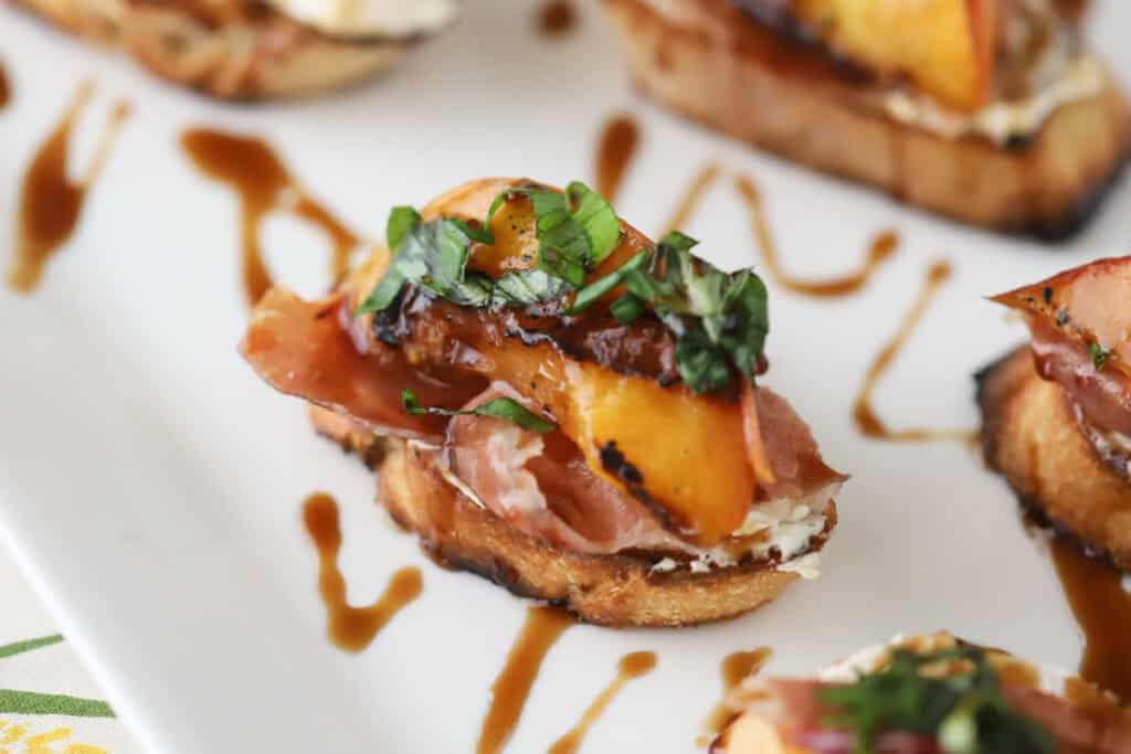 A serving plate with this peach crostini recipe topped with a drizzle of balsamic glaze.