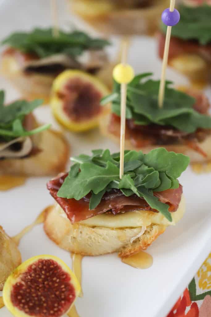 Brie and Fig Crostini topped with prosciutto and fresh arugula on a plate.