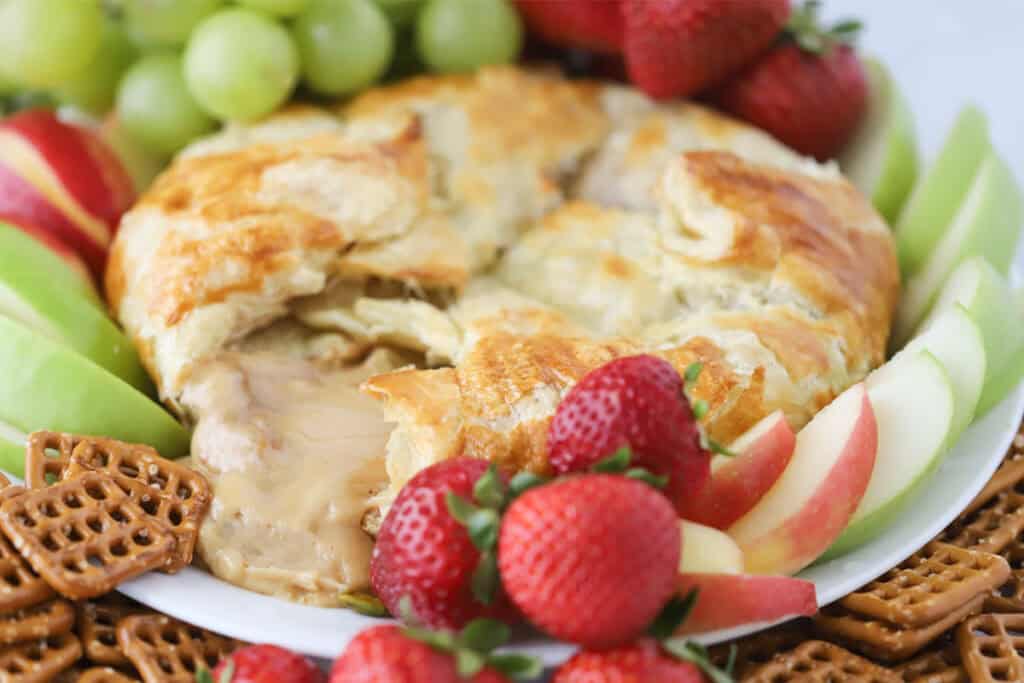 A serving platter with caramel cream cheese puff pastry in the center, surrounded by pretzels and fruit for dipping.