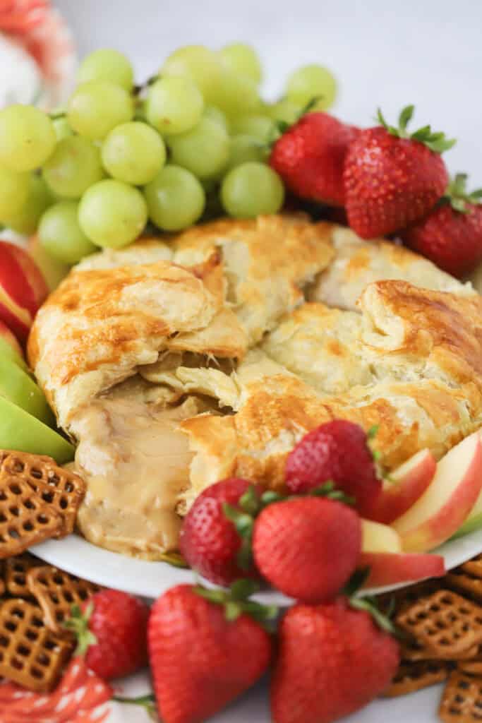 A baked Cream Cheese Puff Pastry round with gooey caramel cheese pouring out, surrounded by fruit and crackers for dipping.