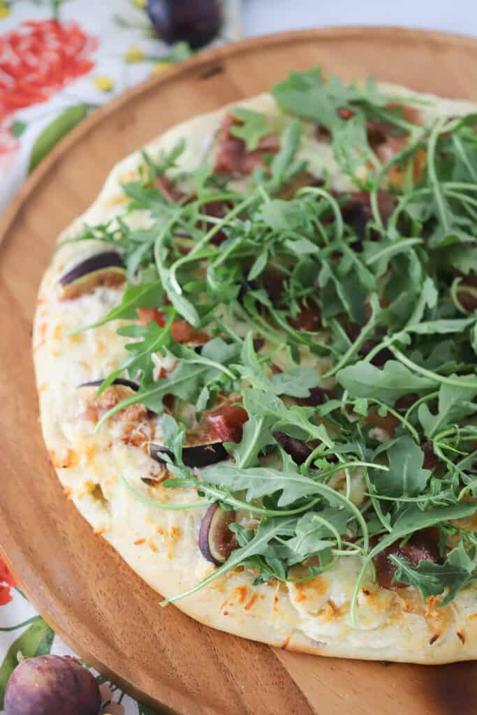 A full homemade pizza topped with figs, prosciutto, and fresh arugula.