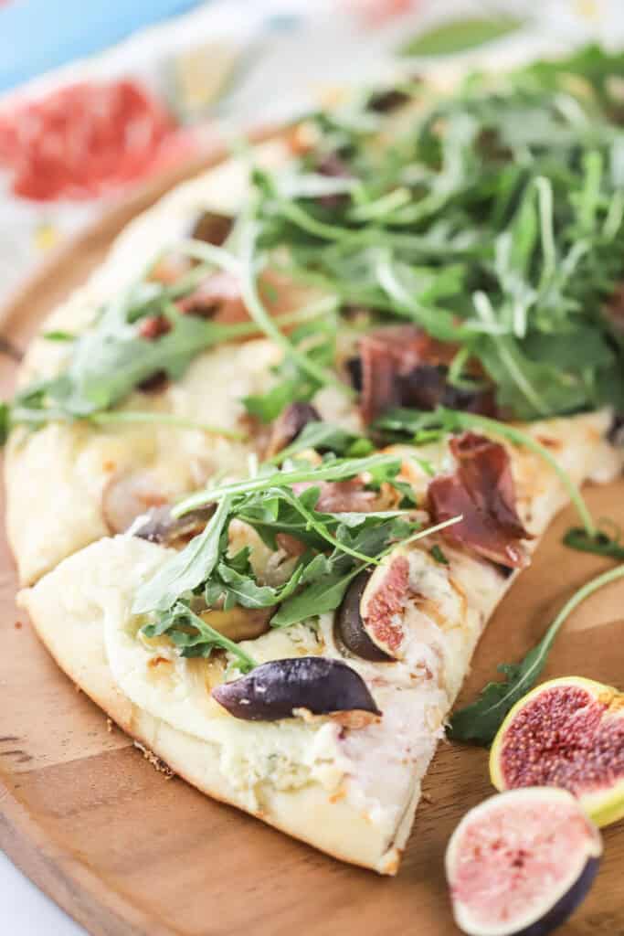 A cutting board with slices of fig and prosciutto pizza topped with fresh arugula.