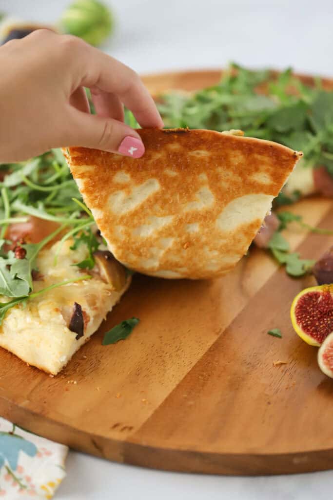 A hand grabbing a slice of prosciutto and fig pizza.