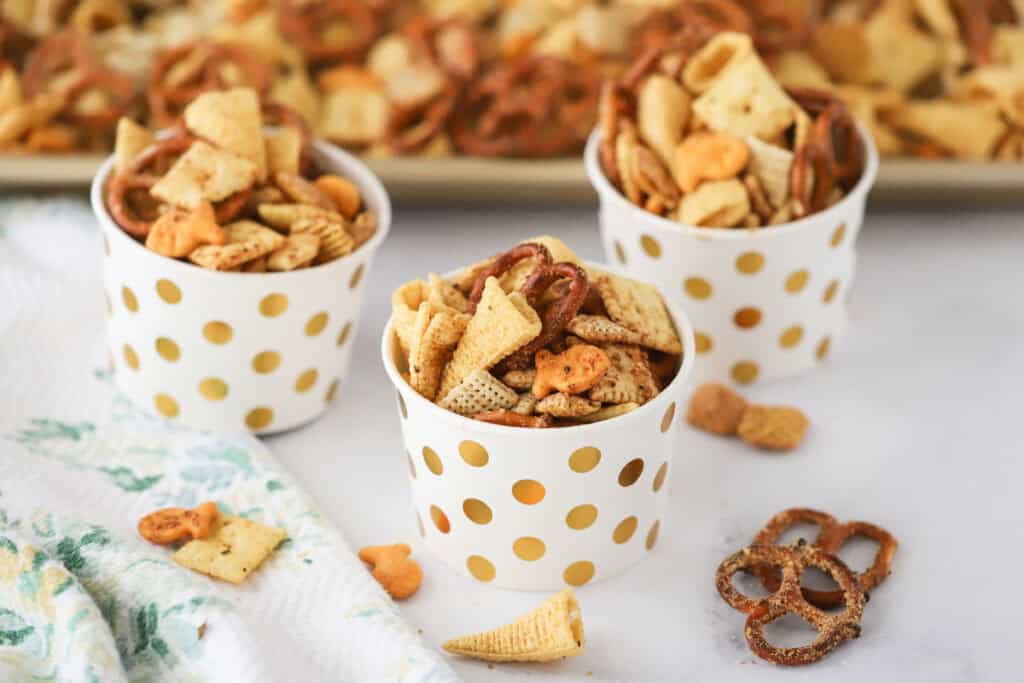 Small cups filled with ranch snack mix including pretzels, rice chex, and bugles crackers.