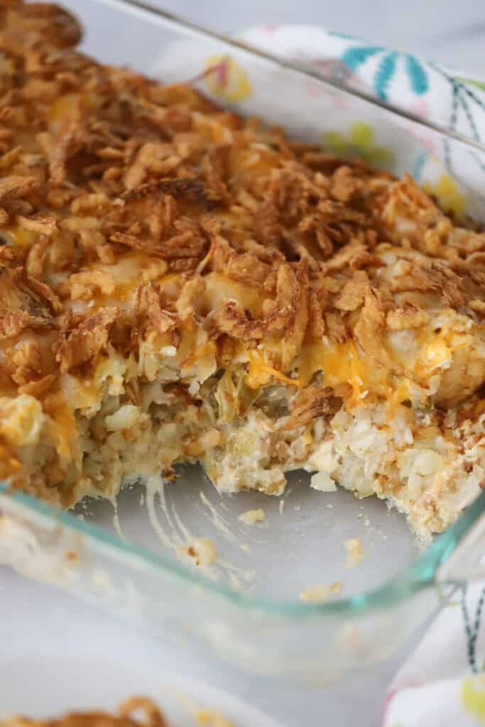 A baking dish full of cheesy tater tot casserole topped with friend onions and cheese.