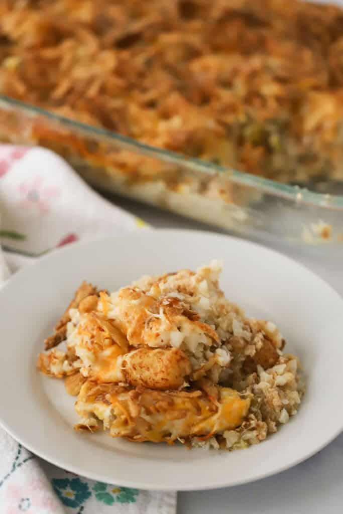 A white dinner plate with cheesy tater tot casserole filled with spicy green chilis and topped with French's fried onions.