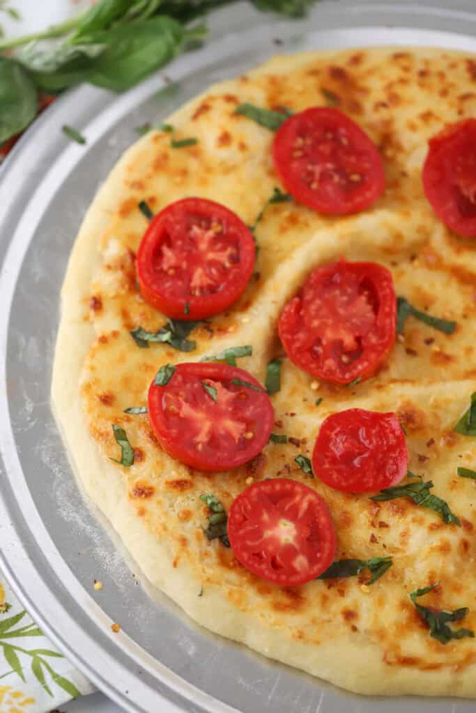 Bianca pizza topped with fresh basil and sliced tomatoes.