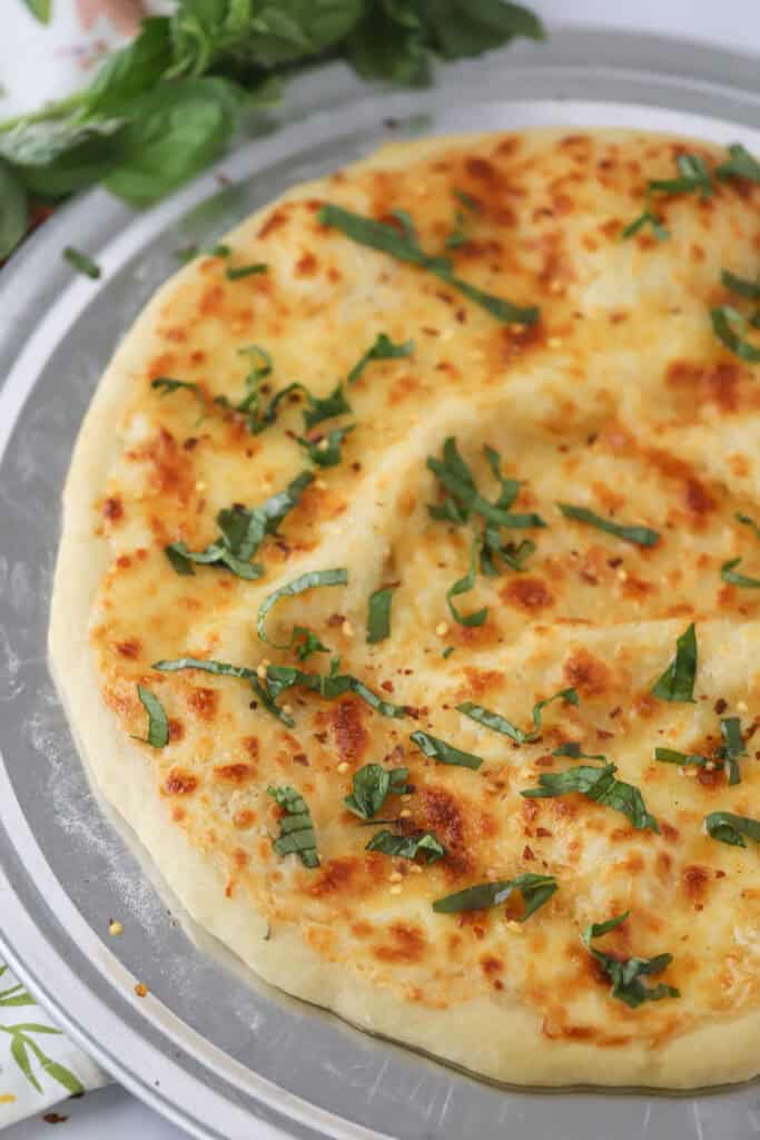 A large white pizza on a round pizza pan topped with sliced basil.