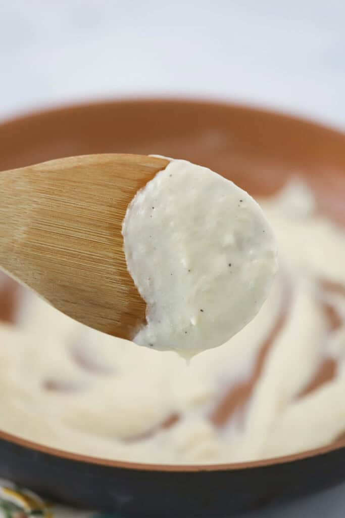 A bowl with white pizza sauce and a wooden spoon coated in the sauce.