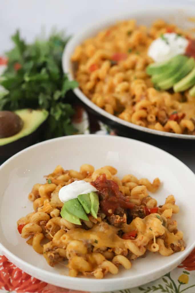 A serving bowl full of this cheesy one pot taco pasta, topped with sour cream and avocados.